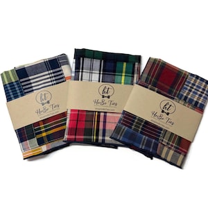 May include: Three plaid handkerchiefs in shades of blue, red, green, and yellow are displayed. Each is wrapped with a brown paper band featuring the text "HoBo Ties" and a logo. The handkerchiefs are arranged on a white background.