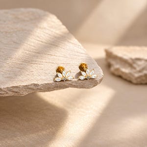 Op de afbeelding: Een paar goudkleurige oorknopjes met een waaiervormig ontwerp. Elke oorbel is versierd met vijf heldere, marquise-geslepen stenen in een stralend patroon, bevestigd met een platte, ronde achterkant voor een stevige pasvorm.