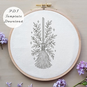 May include: A circular wooden embroidery hoop containing white fabric with a black line art design of a broomstick surrounded by floral branches and small four-pointed stars. The text PDF Template Download is visible in the upper left corner.