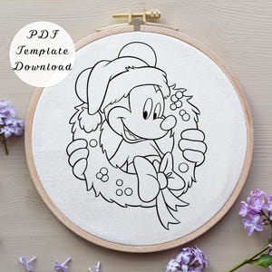 May include: A circular wooden embroidery hoop containing white fabric with a black line art illustration of a cartoon mouse wearing a Santa hat and holding a holiday wreath with a bow. The text PDF Template Download is visible in the corner.
