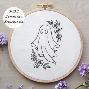 May include: A circular wooden embroidery hoop containing white fabric with a black line art design of a ghost surrounded by floral elements. The text PDF Template Download is visible in the upper left corner of the image.