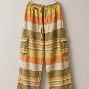 Könnte beinhalten: Weite Cargohose mit horizontalem Streifenmuster in Olivgrün, Senfgelb, Orange und Creme. Die Hose verfügt über einen elastischen Bund mit braunem Kordelzug, zwei seitliche Cargotaschen mit Klappen und eine lockere Passform für bequemes Tragen.