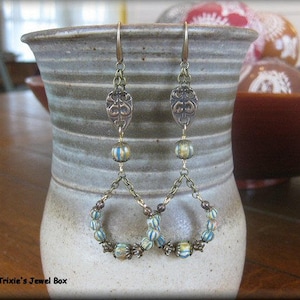 May include: A pair of dangle earrings with a gold chain and blue and white beads. The earrings feature a decorative metal charm at the top.
