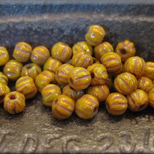 May include: A group of yellow and purple striped glass beads. The beads are arranged in a pile on a brown surface.