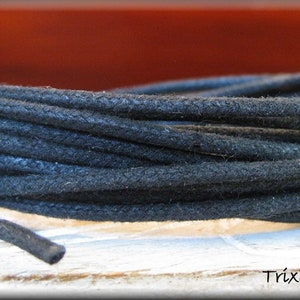 May include: A close-up of a spool of black waxed cotton cord. The cord is tightly wound and has a smooth, polished finish.