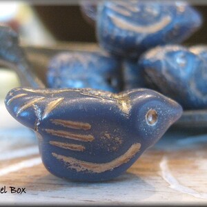 May include: Close-up of several navy blue bird-shaped beads with gold accents. The beads have a distressed, vintage appearance. The beads are likely for jewelry making or crafting. The text "Trixie's Jewel Box" is in the bottom left corner.