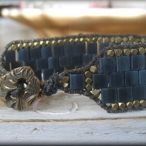 Puede incluir: Un brazalete de cuentas azul oscuro y dorado con un diseño tejido y un cierre de metal decorativo.