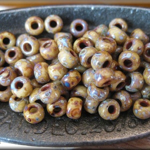 May include: A close-up of a bowl filled with small, round, brown and white ceramic beads. The beads have a speckled pattern and a brown hole in the centre.