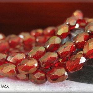 May include: A strand of red faceted glass beads. The beads are oval shaped and have a metallic sheen.
