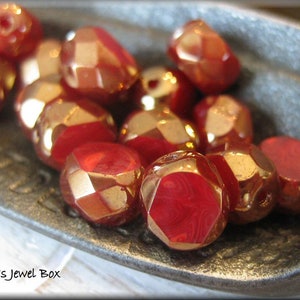 May include: A close-up of a group of red and gold faceted glass beads. The beads are arranged in a pile on a metal surface.