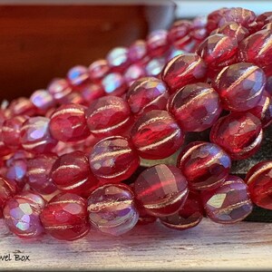 May include: A strand of red glass beads with gold accents. The beads are faceted and have a slightly iridescent finish.