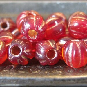 May include: A collection of red glass beads with gold flecks. The beads are round and have a slightly textured surface.
