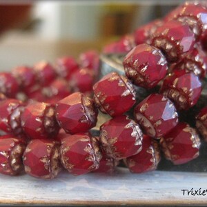 May include: A close-up of a strand of red glass beads with gold accents. The beads are faceted and have a shiny finish.