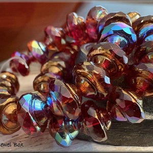 May include: Close-up of a strand of faceted beads in shades of red, amber, and iridescent blue. The beads are arranged in a spiral pattern. The image includes the text "Trixie's Jewel Box".