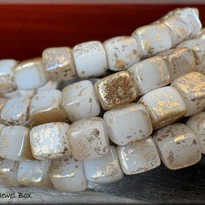 May include: A strand of white square glass beads with gold flecks. The beads are approximately 1/2 inch in size.