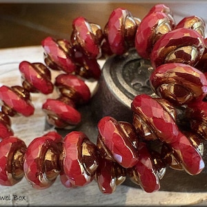 May include: Strand of faceted red and gold beads. The beads have a faceted, geometric design and are strung together on a clear string. The beads are a deep red color with gold accents. The beads are arranged in a curved shape.