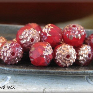 May include: A close-up of a group of red glass beads with gold accents. The beads are arranged in a semi-circle on a dark grey surface.