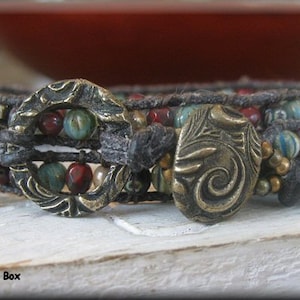 May include: A multi-strand bracelet with brown leather cord, red, green, and white beads, and two ornate metal clasps.