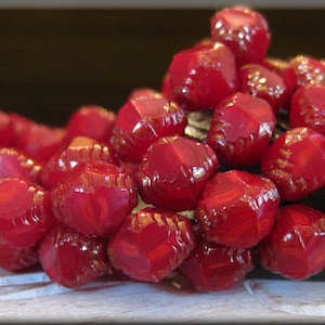 May include: A strand of red glass beads with a faceted, hexagonal shape. The beads have a slight gold shimmer.