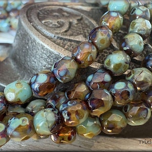 May include: A strand of iridescent glass beads with a mix of teal, brown, and gold colors. The beads have a faceted, irregular shape.