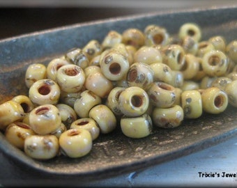 May include: A close-up of a bowl filled with small, round, cream-colored beads with brown speckles. The beads are arranged in a random pattern.