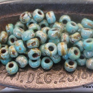 May include: A close-up of a pile of turquoise blue and brown glass beads. The beads are small and round, with a hole in the center. They are arranged in a random pattern.