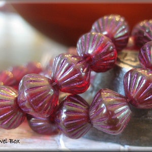 May include: A strand of deep red glass beads with a scalloped design. The beads have a subtle iridescent sheen.