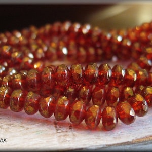 May include: A strand of red faceted glass beads with a metallic sheen. The beads are arranged in a circular pattern and are stacked on top of each other.