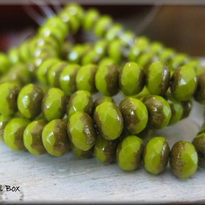 May include: A strand of lime green glass beads with a gold metallic finish. The beads are faceted and have a slightly irregular shape.