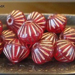 May include: A close-up of a group of red glass beads with a faceted, starburst design. The beads are arranged in a bowl.