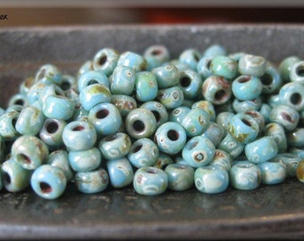 May include: A close-up of a pile of small, round, turquoise beads with white speckles. The beads are arranged in a random pattern and are all the same size. The beads are on a metal surface.