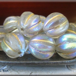 May include: A group of iridescent glass beads with gold accents. The beads are round and have a textured surface. They are arranged in a pile on a dark gray surface.