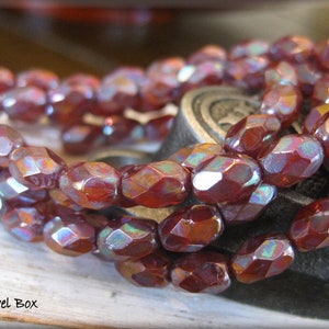 May include: Strands of faceted, reddish-brown beads with iridescent highlights. The beads have an oval shape and are strung together, creating a necklace or bracelet. The beads are displayed on a light-colored surface.