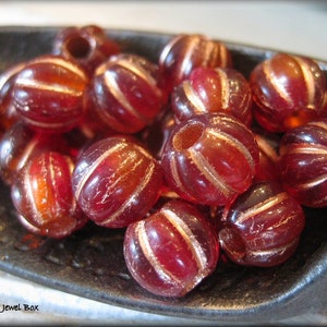 May include: A collection of red and gold glass beads with a striped pattern. The beads are arranged in a bowl.