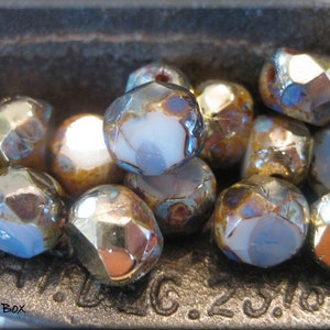 May include: A close-up of a collection of iridescent glass beads in shades of blue, gold, and brown. The beads have a faceted, geometric shape and are arranged in a bowl.