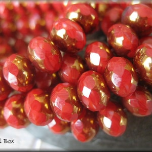 May include: A close-up of a strand of red and gold glass beads. The beads are faceted and have a metallic sheen.