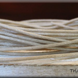 May include: A close-up of a spool of beige waxed cord. The cord is wound tightly and has a smooth, slightly textured surface.