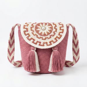 May include: A pink crossbody bag with a white and pink patterned strap. The bag features a decorative flap with a beaded design and two tassels. The bag is approximately 8 inches tall and 7 inches wide.