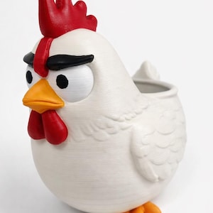 May include: A white ceramic chicken figurine with a red comb, wattle, and beak. The chicken has black eyebrows and orange feet. The figurine has a small opening on its back, suggesting it could be used as a planter or decorative item.