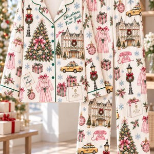 May include: A cream-colored pajama set featuring a button-down long-sleeve shirt and matching pants. The fabric is printed with Christmas in New York motifs, including yellow taxis, The Plaza hotel, Christmas trees, gifts, and pink telephones.