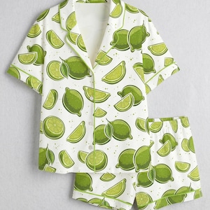 May include: White pajama set with a lime fruit pattern. The set includes a short-sleeved button-down shirt and matching shorts. The design features green limes and lime slices on a white background, with green trim.