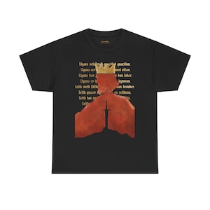 Könnte beinhalten: Ein schwarzes T-Shirt mit kurzen Ärmeln und einer Grafik, die eine rote Silhouette einer gekrönten Figur zeigt, die hinter einem im Boden steckenden Schwert steht. Hinter der Figur befindet sich ein Textblock in dunkler Schrift. Rundhalsausschnitt.