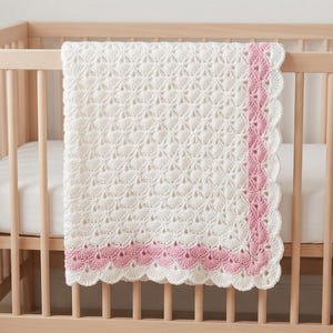 May include: A rectangular crochet blanket featuring a white textured shell stitch pattern throughout the centre. The blanket is finished with a decorative border consisting of a row of pink shell stitches followed by a final row of white shell stitches.