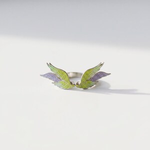 Close-up of angel wing enamel ring, showing the colorful enamel details and silver open band