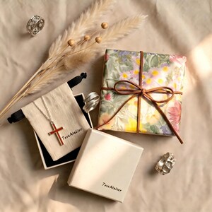 Pu&ograve; includere: Un assortimento di gioielli e regali, tra cui anelli, una collana con pendente a croce e un regalo confezionato. La collana presenta una croce rossa. Il regalo &egrave; avvolto in carta floreale e legato con un nastro marrone. Il marchio "Tove Atelier" &egrave; visibile.