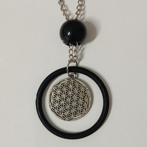 May include: A silver-toned pendant necklace featuring a black rubber ring and a circular pendant with a geometric flower of life design. The necklace has a black bead and a silver chain.