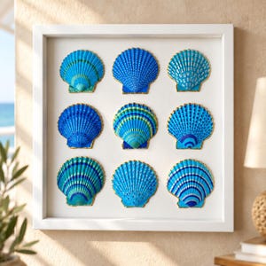 Pode incluir: Uma moldura quadrada branca contendo nove conchas de vieira individuais dispostas numa grelha de três por três. Cada concha é pintada em vários tons de azul e verde com bordas douradas, sobre um fundo branco liso.