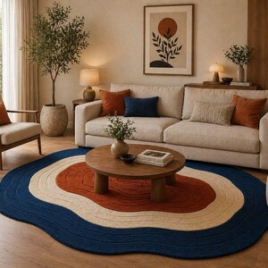 Könnte beinhalten: Ein Wohnzimmer mit einem cremefarbenen Sofa, orangefarbenen und blauen Kissen und einem runden Couchtisch aus Holz. Ein blauer, orangefarbener und cremefarbener Teppich liegt auf dem Boden. Ein gerahmtes Kunstwerk und ein Topfbaum ergänzen die Einrichtung.