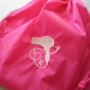 May include: A pink drawstring bag with a white embroidered design of a hairdryer and the letters "SOR".