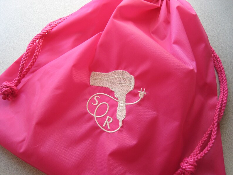 May include: A pink drawstring bag with a white embroidered design of a hairdryer and the letters "SOR".